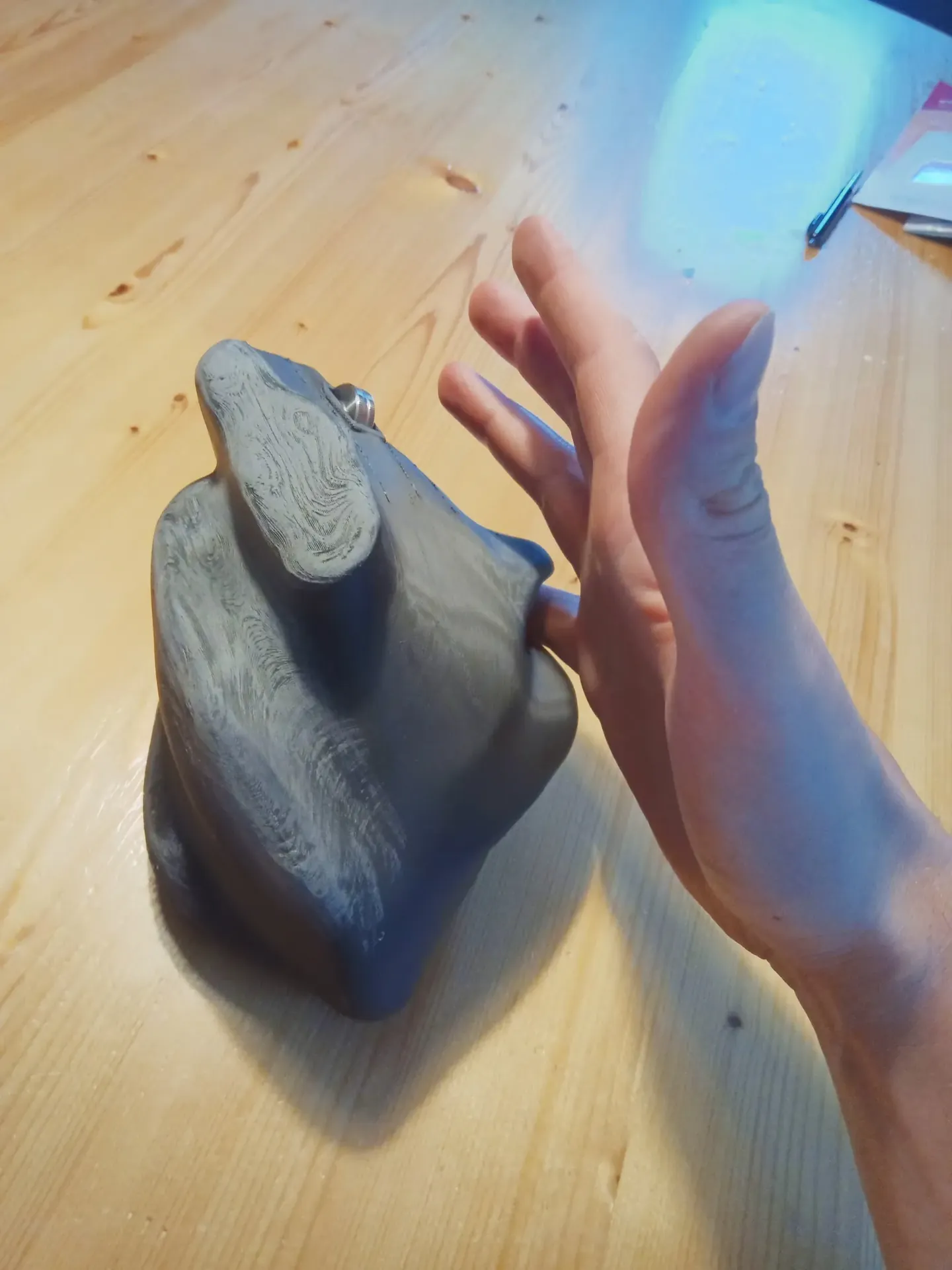 The finished 3D printed mouse on a wooden desk next to the open hand it was shaped for